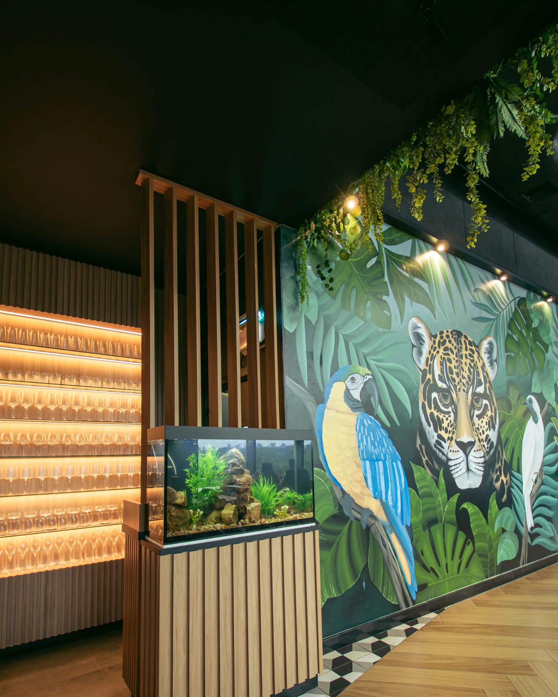 Barra con estanterías de copas retroiluminadas, el acuario y el mural de la selva