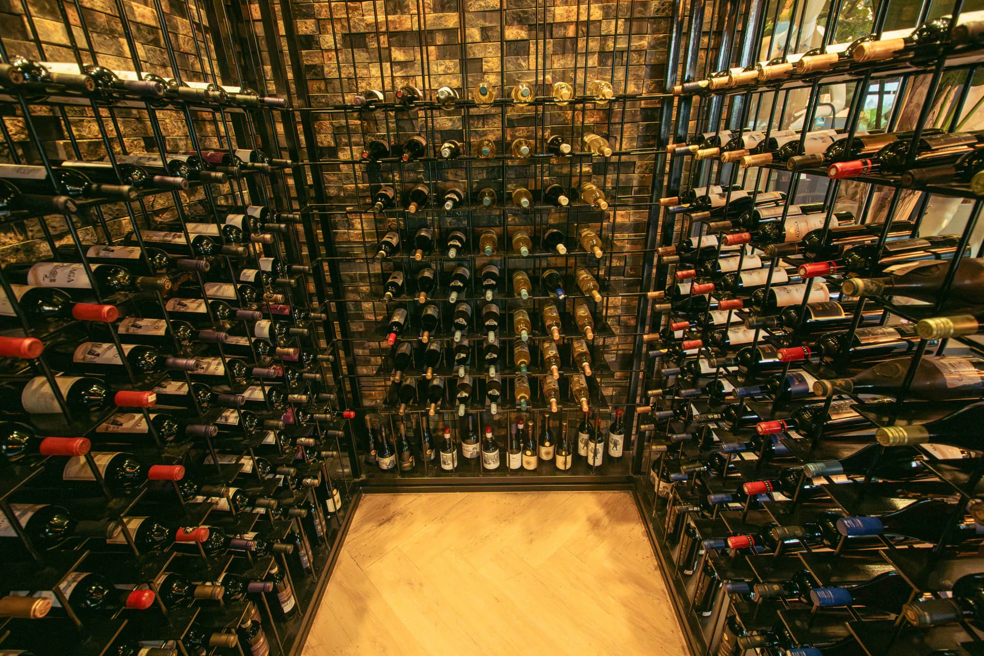 Interior de la cava con botellas en estanterías de hierro bajo luz ámbar